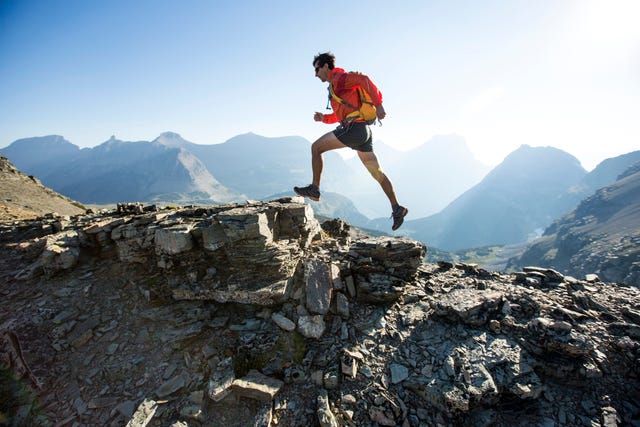 man loopt hard op rotsachtige bergkam met bergen op achtergrond