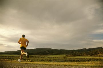 man running on rural road, rear view, summer