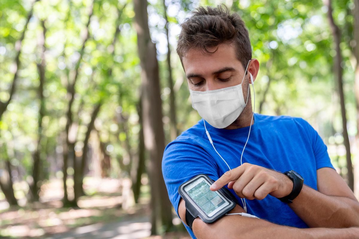 man running outdoors wearing a facemask and using an arm band for his cell phone