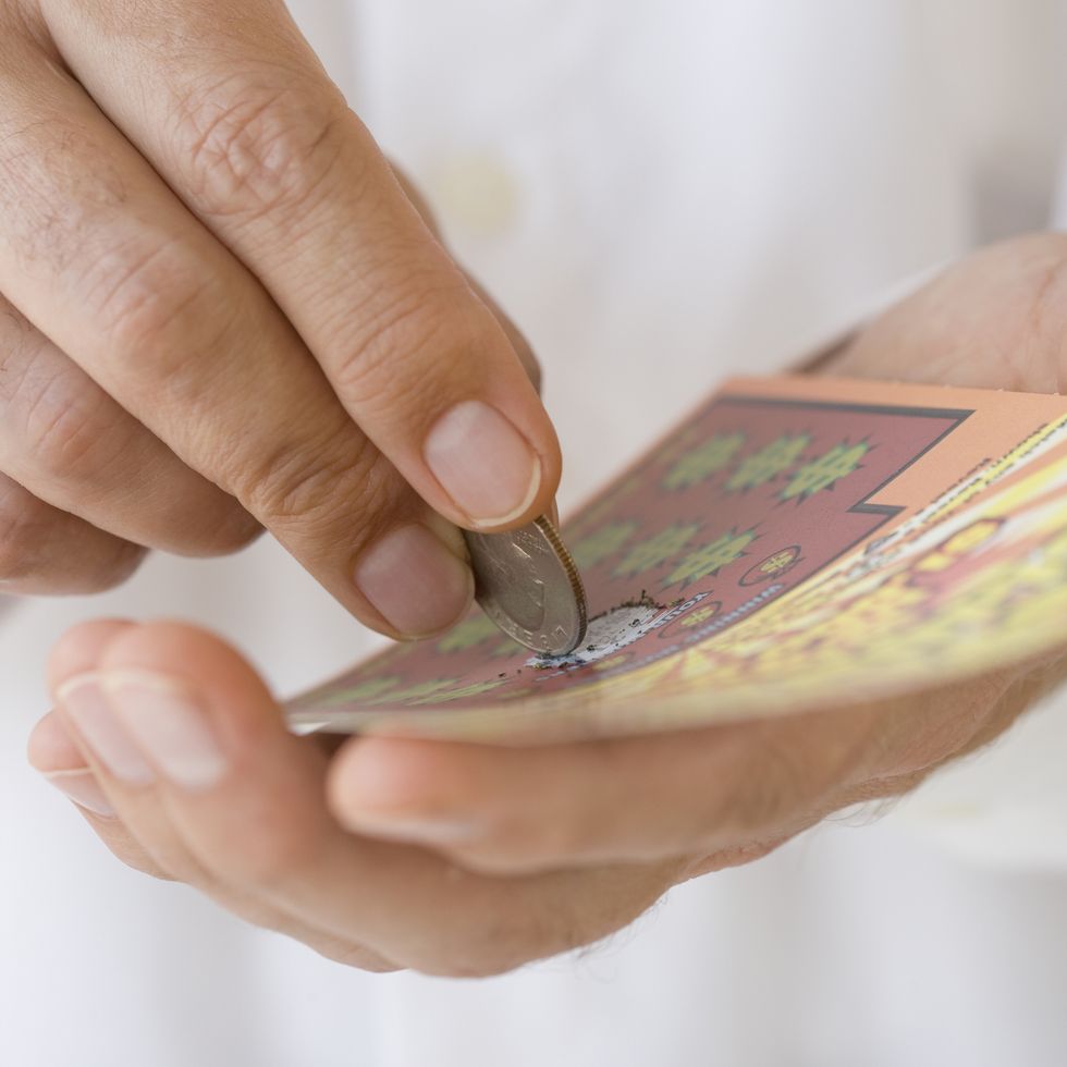 man scratching lottery card with coin