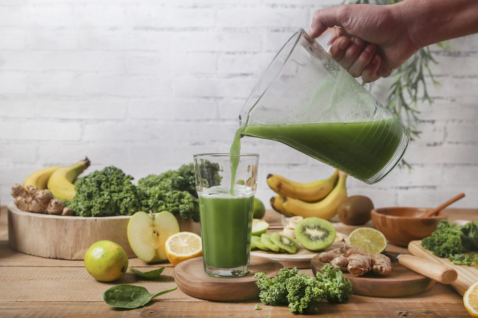 man serving glass of green smoothie surrounded by ingredients