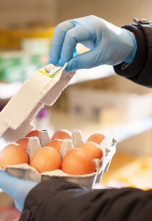 Man shopping for eggs at supermarket, wearing protective gloves