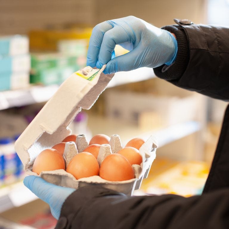 Man shopping for eggs at supermarket, wearing protective gloves