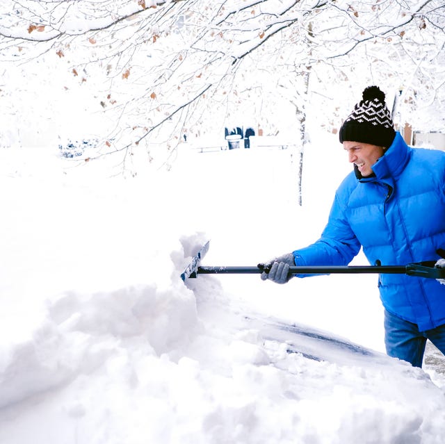 man shovels snow from car in driveway after winter storm