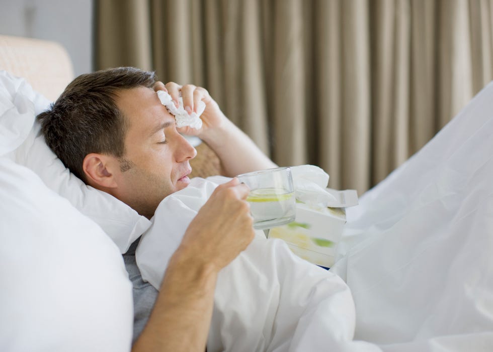 man sick in bed drinking hot drink