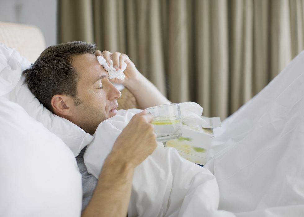 man sick in bed drinking hot drink