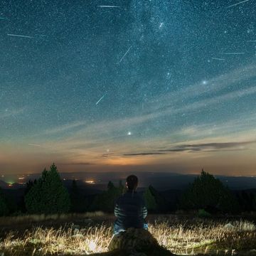 een man zit op een berg en kijkt naar de vallende sterren van de meteorenzwerm perseiden