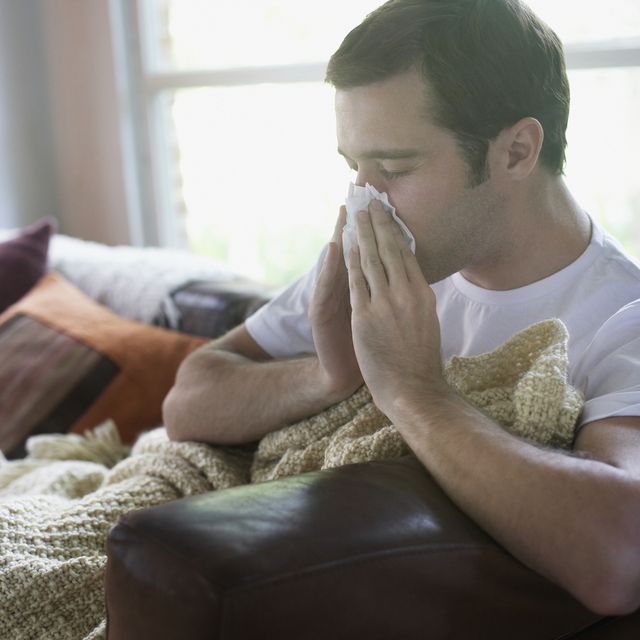 Man sitting in living room blowing nose