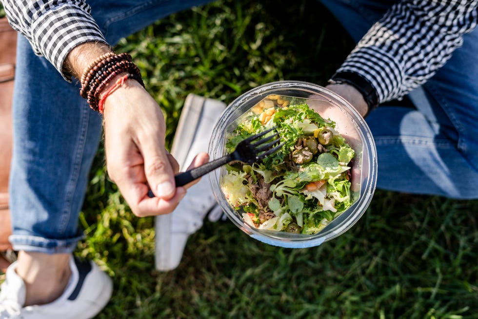 man sitting on a meadow eating mixed salad, partial view