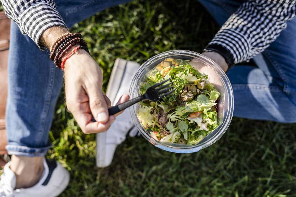 man sitting on a meadow eating mixed salad, partial view