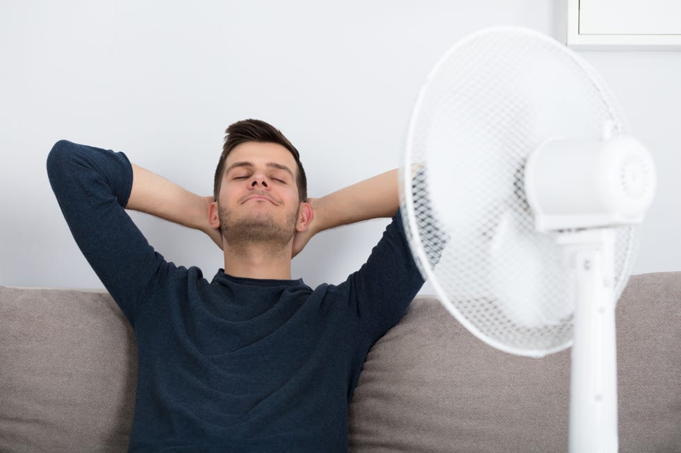 man sitting on couch cooling off with fan