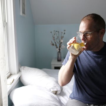 man sitting on side of bed, drinking water with lemon, side view