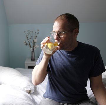 man sitting on side of bed, drinking water with lemon, side view