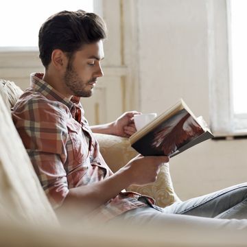 man sitting on sofa reading book