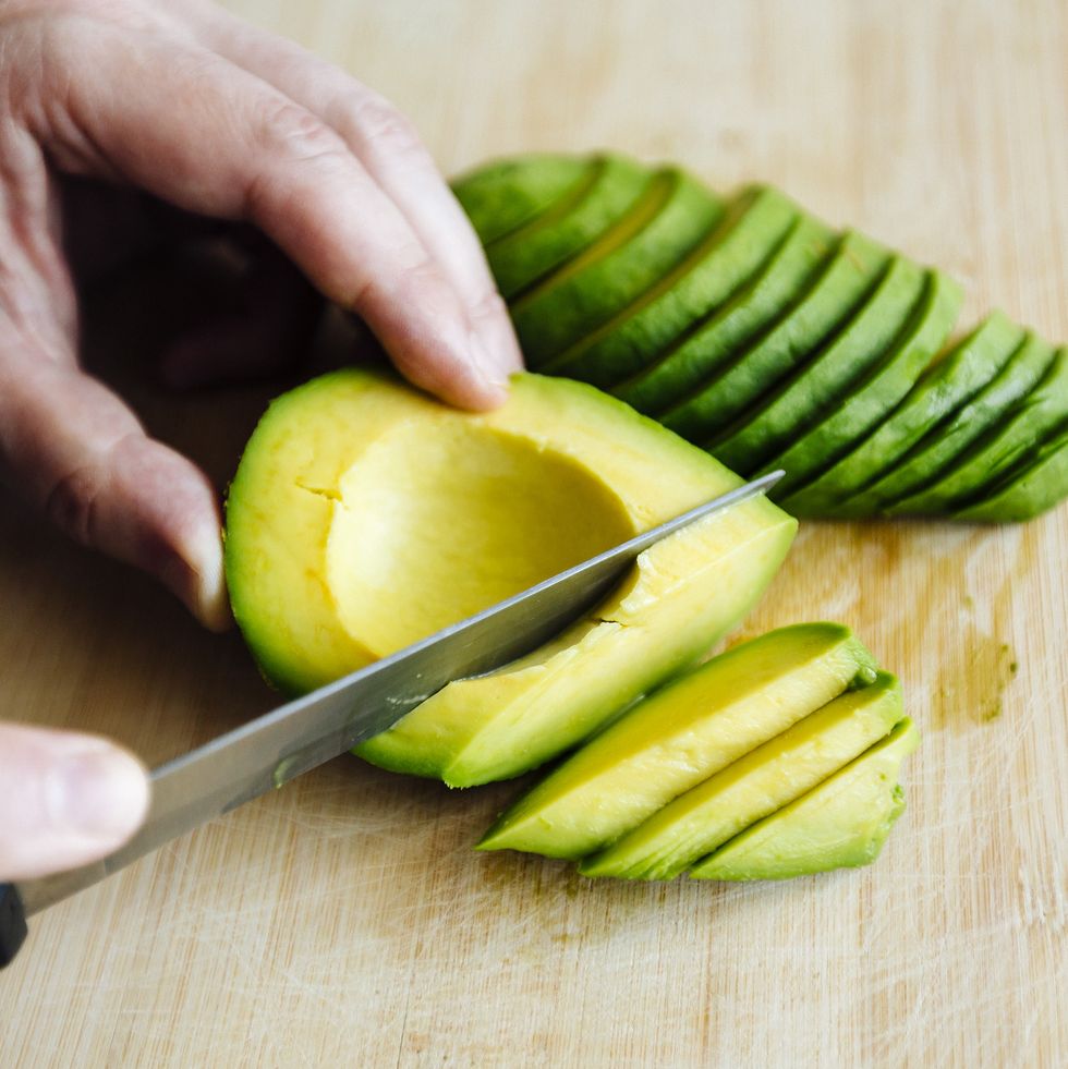 man slicing avocado with a knife on a cutting board close up