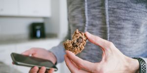 man snacks on cookie while looking at his smart phone