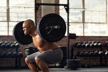 determined african american man lifting weight in gym muscular strong man taking efforts to lift weight barbell in fitness center black shirtless bodybuilder doing squatting with a barbell on shoulder