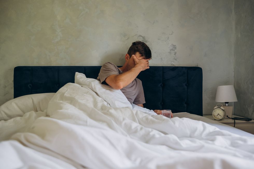 man suffers from a hangover in the morning in bed he holds his hand on his head headache in the morning