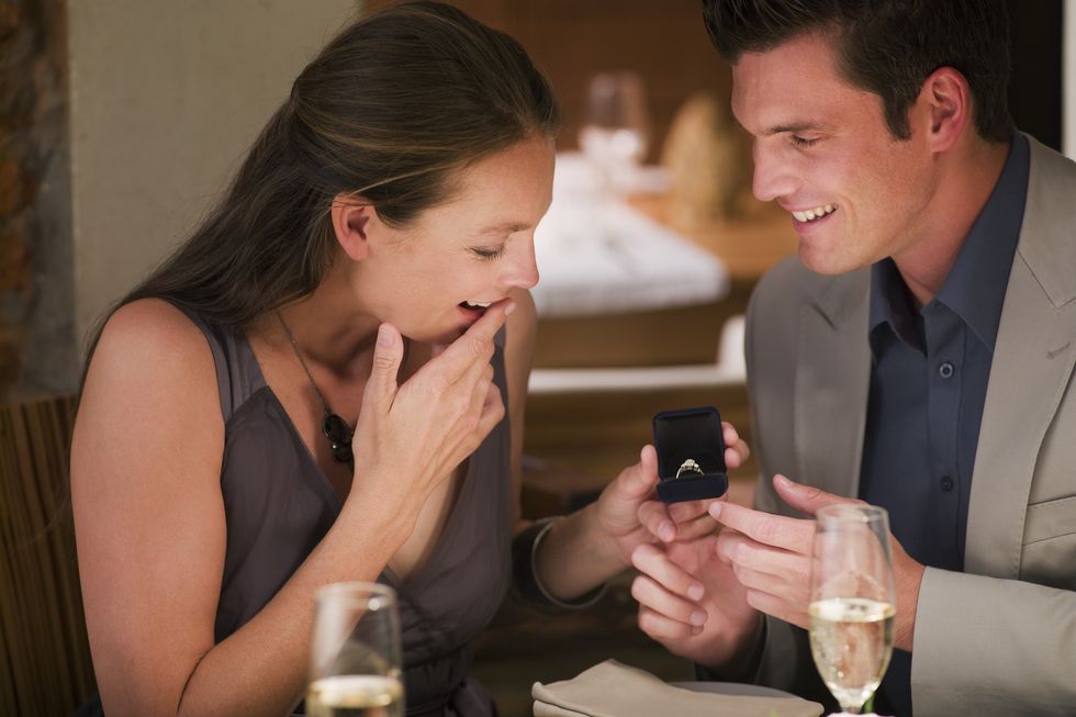 man surprising woman with engagement ring at restaurant table