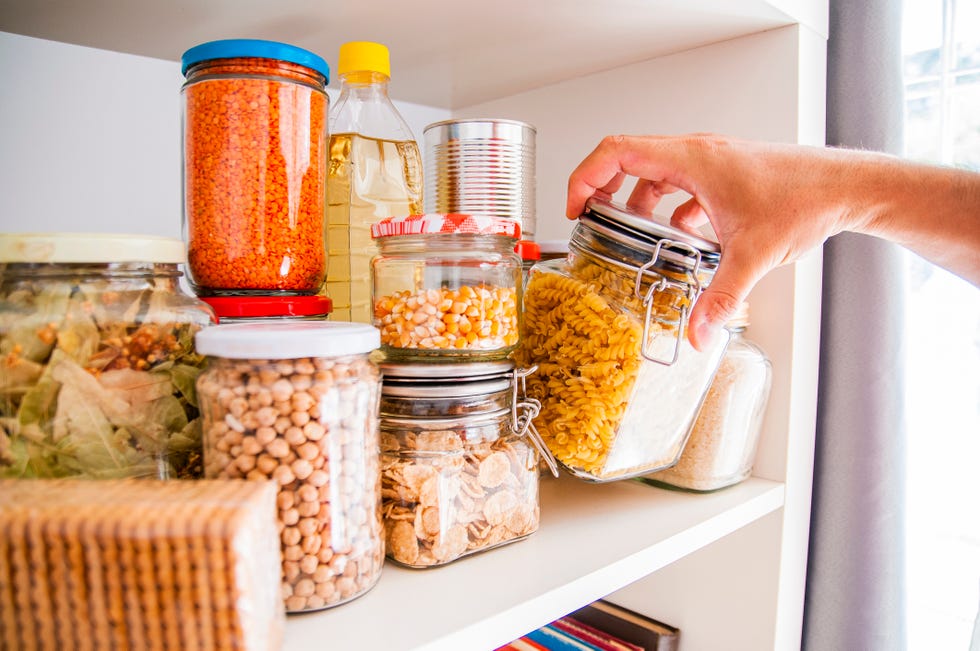 a man takes or places glass jars filled with legumes from a shelf in the pantry