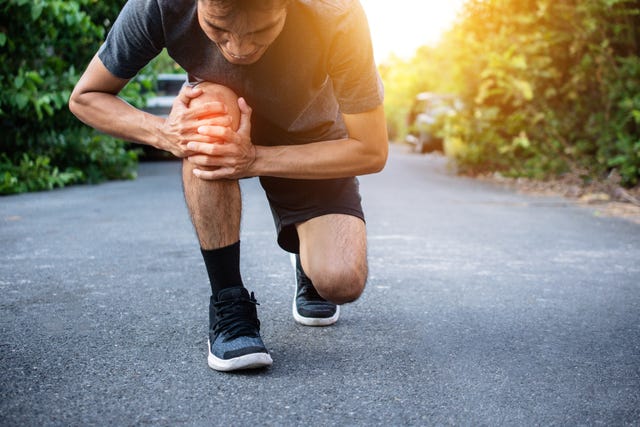 man touching knee in pain on road