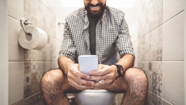 Man zit op telefoon op wc tijdens het poepen en lacht