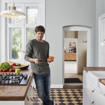 Man using smartphone and holding bell pepper in kitchen