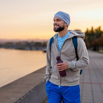 man walking by riverside during sunrise with water bottle held