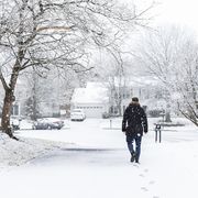 man walking in driveway in neighborhood with snow covered ground during blizzard white storm, snowflakes falling in virginia suburbs, single family homes to check mail in mailbox