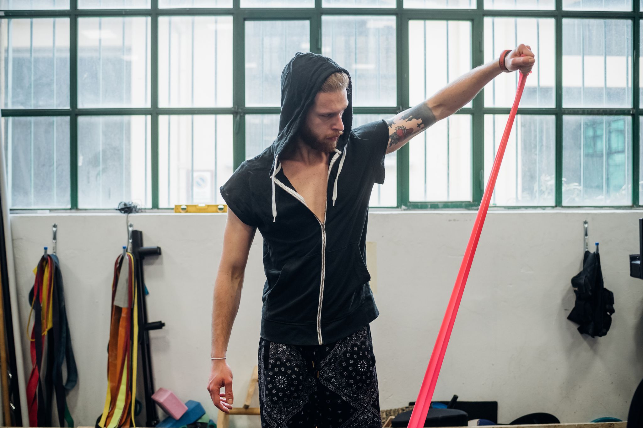 man wearing a black hoodie standing in a gym pulling up an elastic band to head height