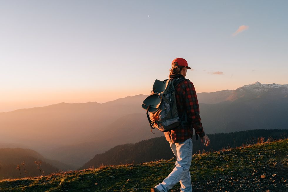 man with a backpack walks in the mountains at sunset