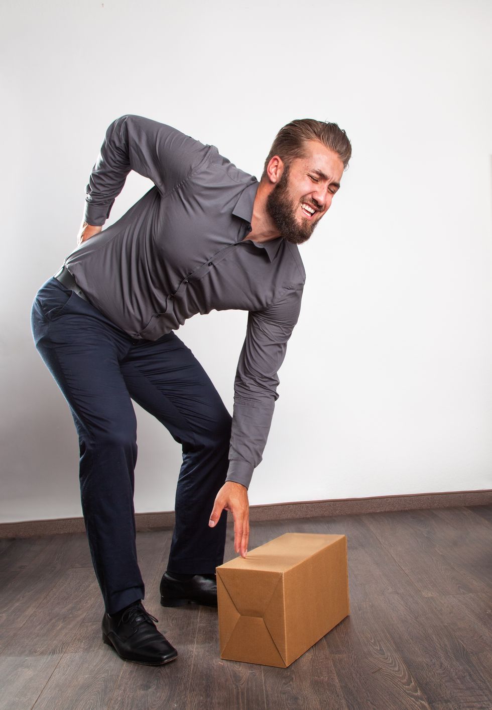 Man With Backache Reaching Box While Bending Against White Wall