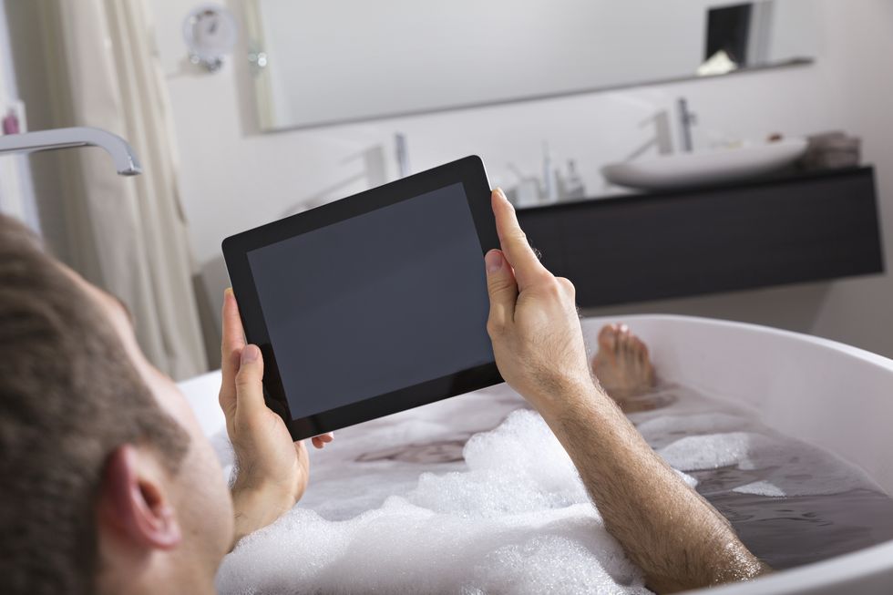 man with digital tablet sitting in bathtub