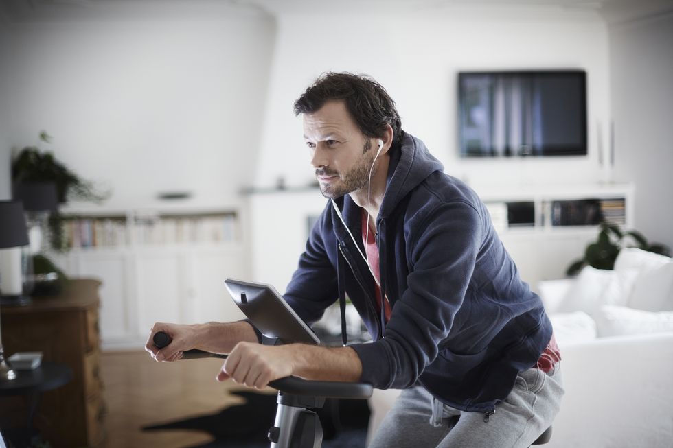 man with earbuds on exercise bike at home