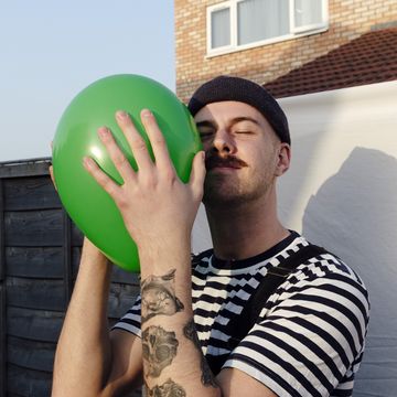 man with eyes closed holding green balloon at back yard