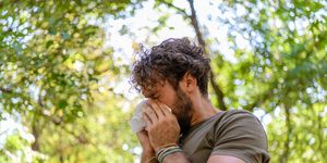 a man with flu is walking in public park and sneezing in paper tissues