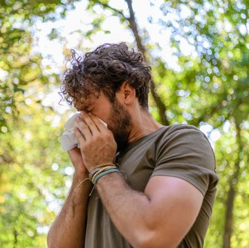 a man with flu is walking in public park and sneezing in paper tissues