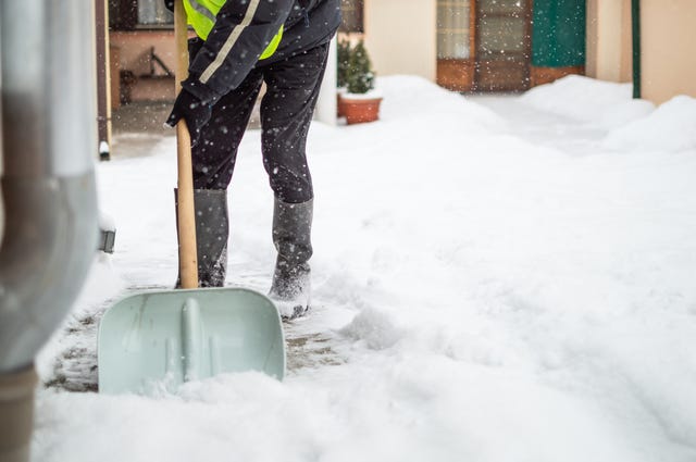 man with snow shovel cleans sidewalk