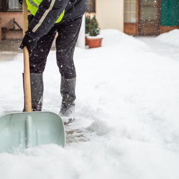 man with snow shovel cleans sidewalk
