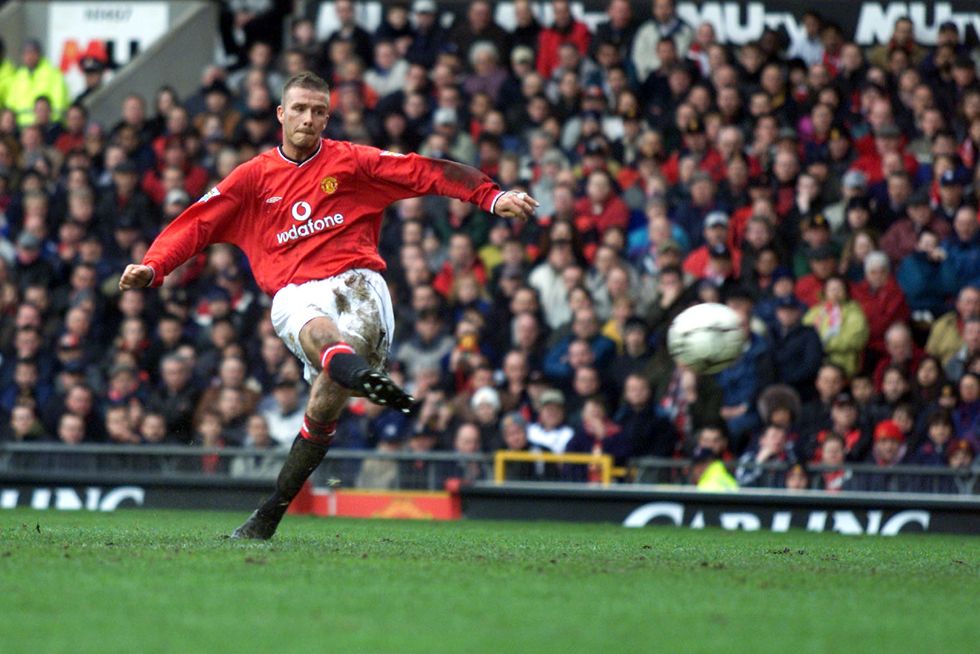 david beckham in a red soccer uniform, kicking a ball during a match