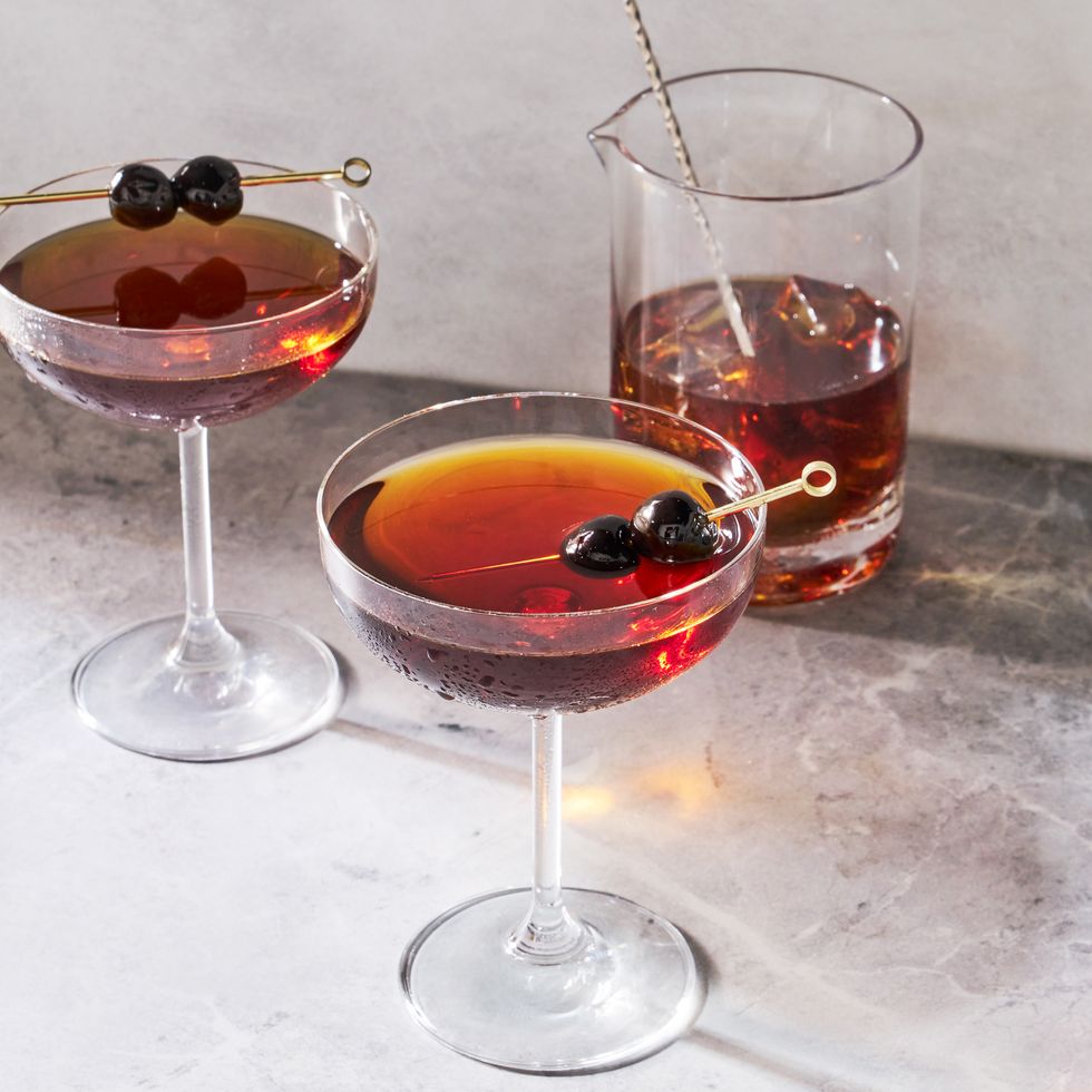 manhattan cocktail in a coupe glass garnished with dark cherries