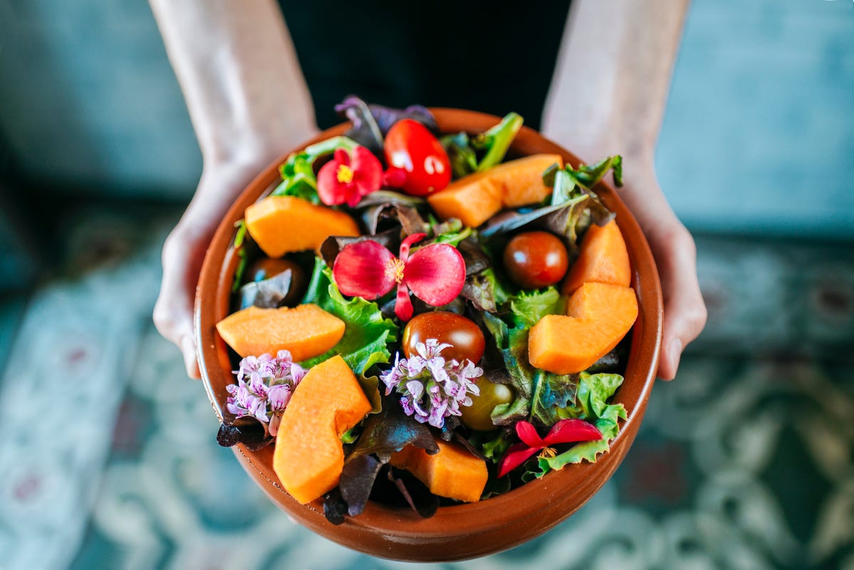 man's hands holding bowl of mixed salad garnished with edible flowers, close up
