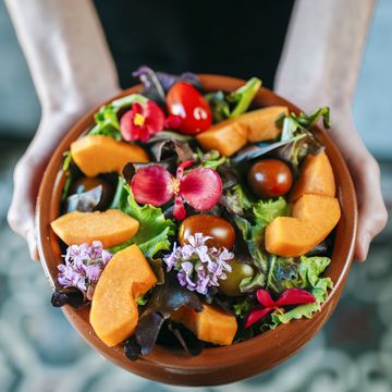 man's hands holding bowl of mixed salad garnished with edible flowers, close up