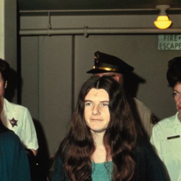 a woman with long hair is escorted down a hallway by officers