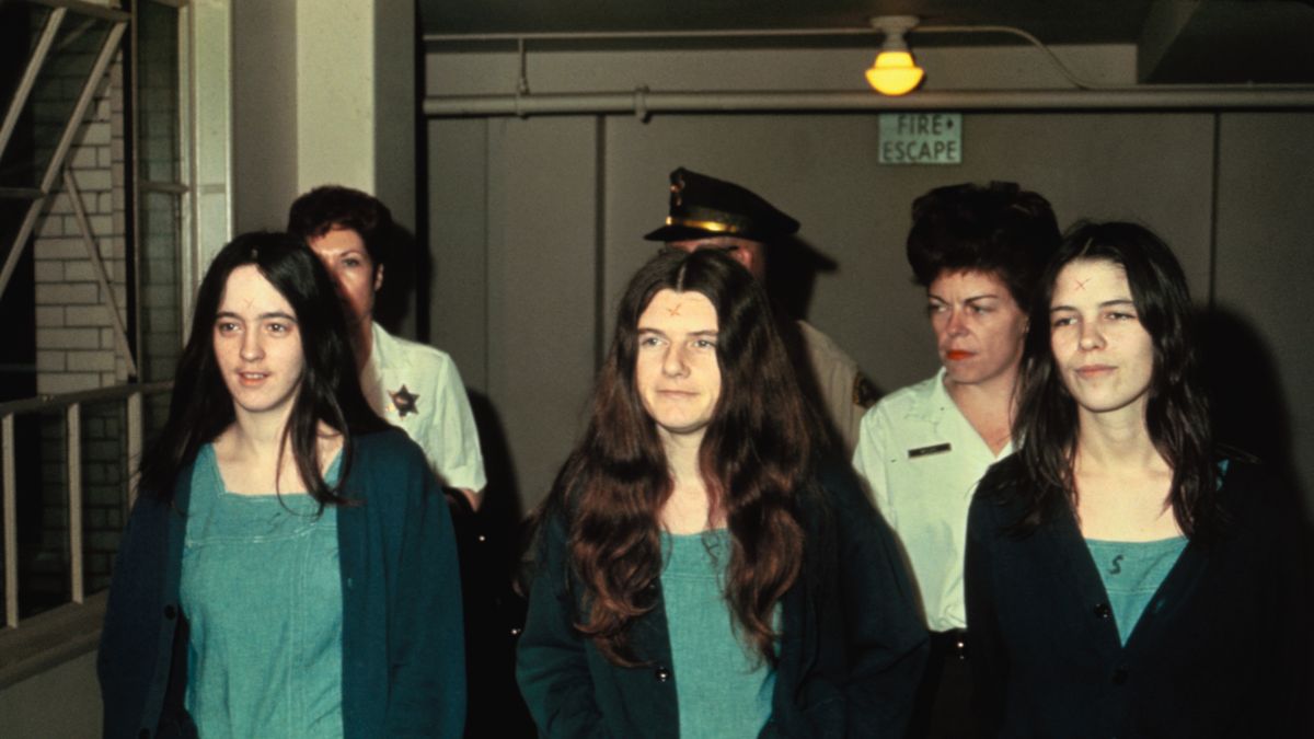 a woman with long hair is escorted down a hallway by officers