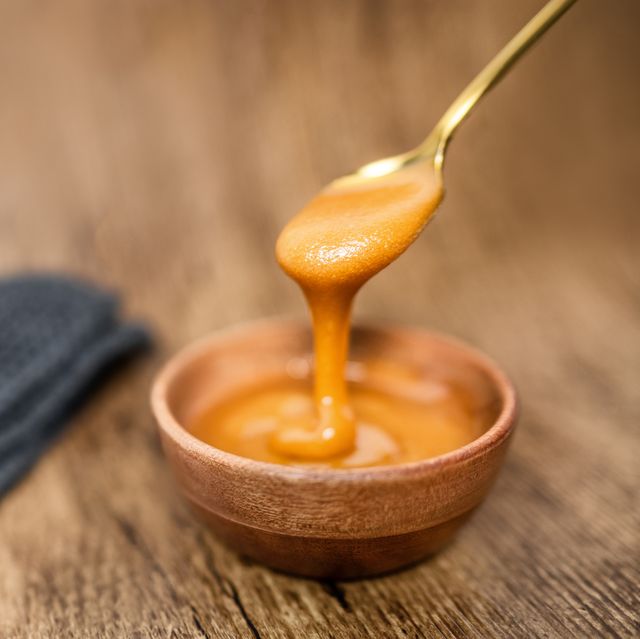 manuka honey from new zealand dripping from golden spoon in wooden bowl showing texture of natural healthy organic raw food