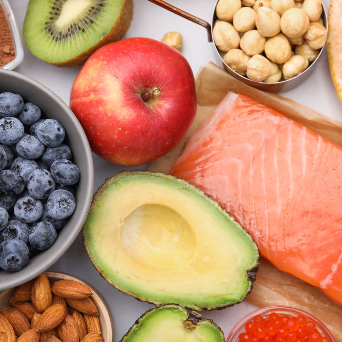 een foto van verschillende gezonde producten, zoals een appel, avocado, blauwe bessen en zalm