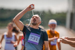 een man gooit de inhoud van zijn bekertje op zijn hoofd tijdens het lopen van een hardloopevent