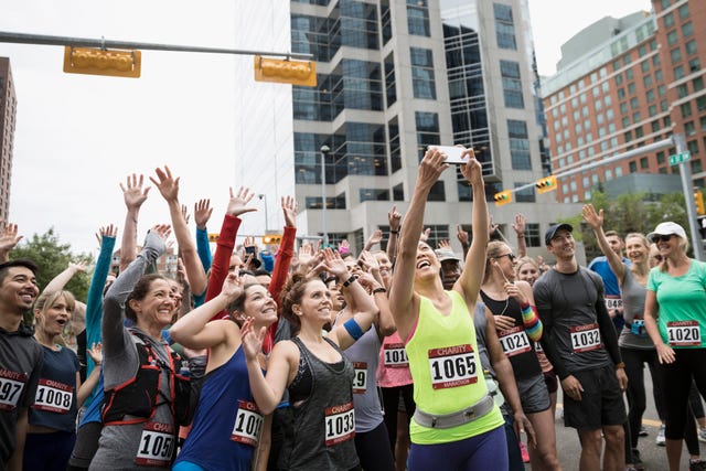 Marathon runners posing, waving and cheering for selfie at starting line on urban street