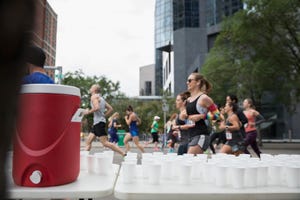 Marathon runners running, passing water station on urban street